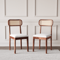 Two wooden chairs with wicker backrests and white cushions on a neutral background