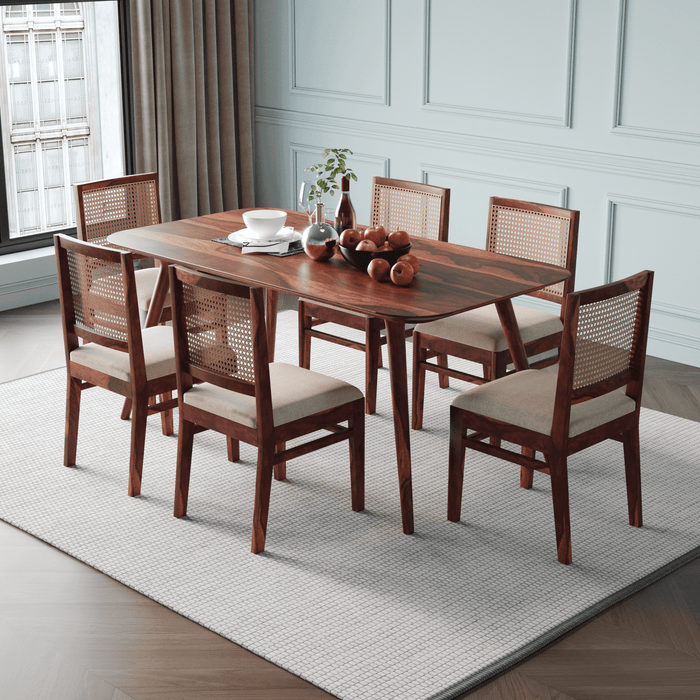 Wooden dining table with six chairs in a room with white walls and a window.