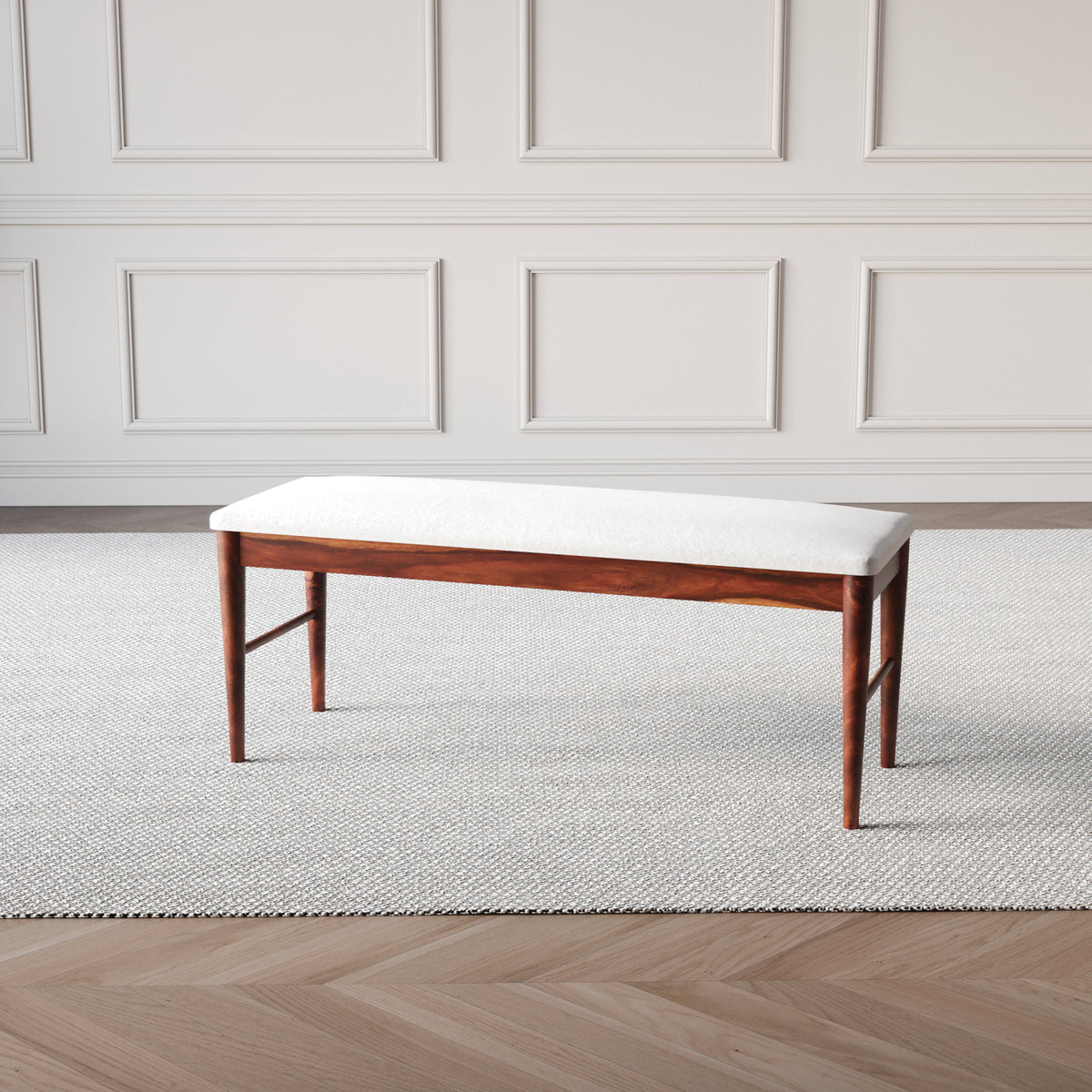 Wooden bench with white cushion against a neutral wall.
