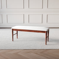 Wooden bench with white cushion against a neutral wall.
