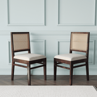 Two wooden chairs with wicker backrests and white cushions against a light blue paneled wall.