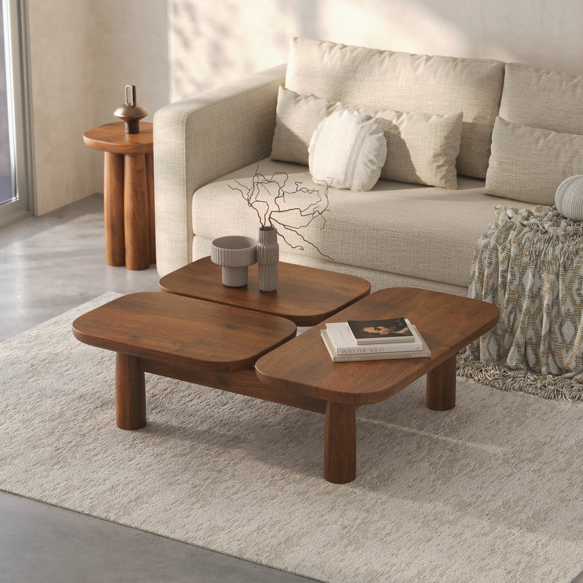 A modern three-piece wooden coffee table set in a bright, contemporary living room with a beige sofa and textured rug.