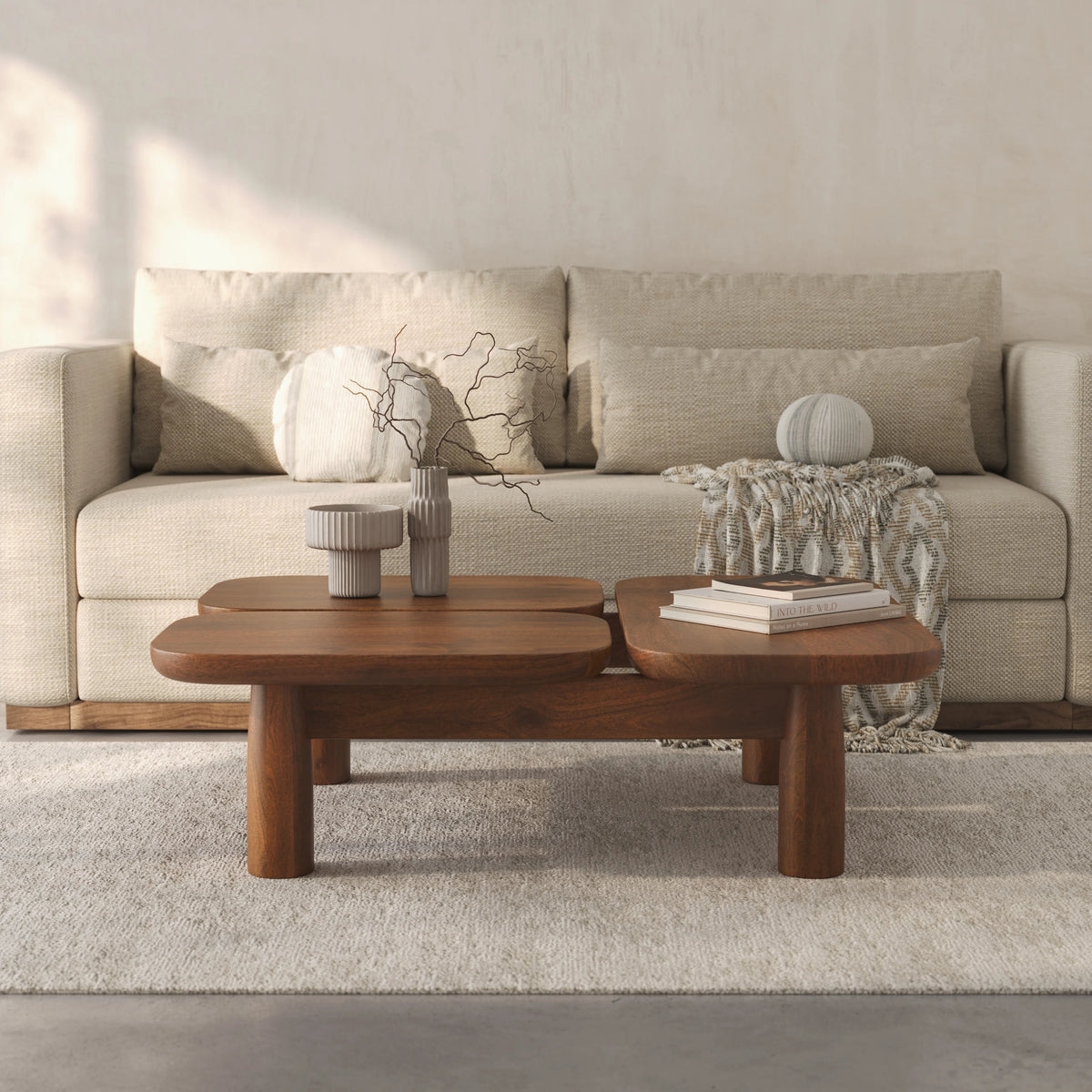 A modern two-tier wooden coffee table in a warm medium brown finish, styled in a minimalist living room setting with a beige sofa, neutral throw pillows, a textured throw blanket, and decorative ceramic vases.