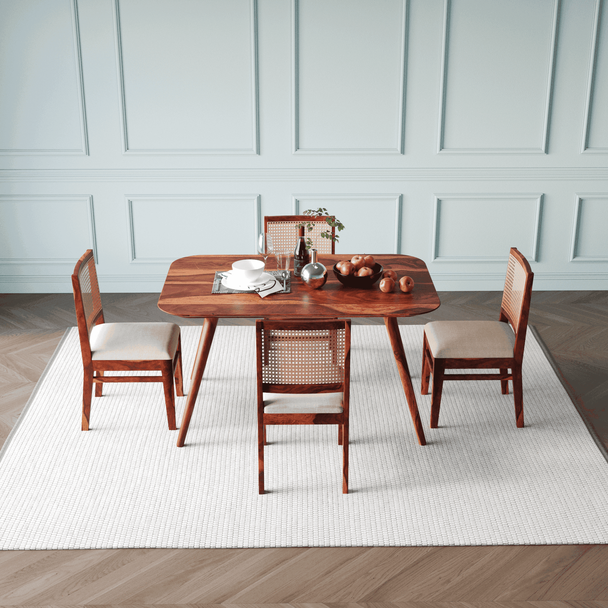 Wooden dining table with four chairs in a room with light blue paneled walls.