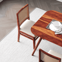 Wooden dining table with chairs on a white rug in a room with wooden flooring.