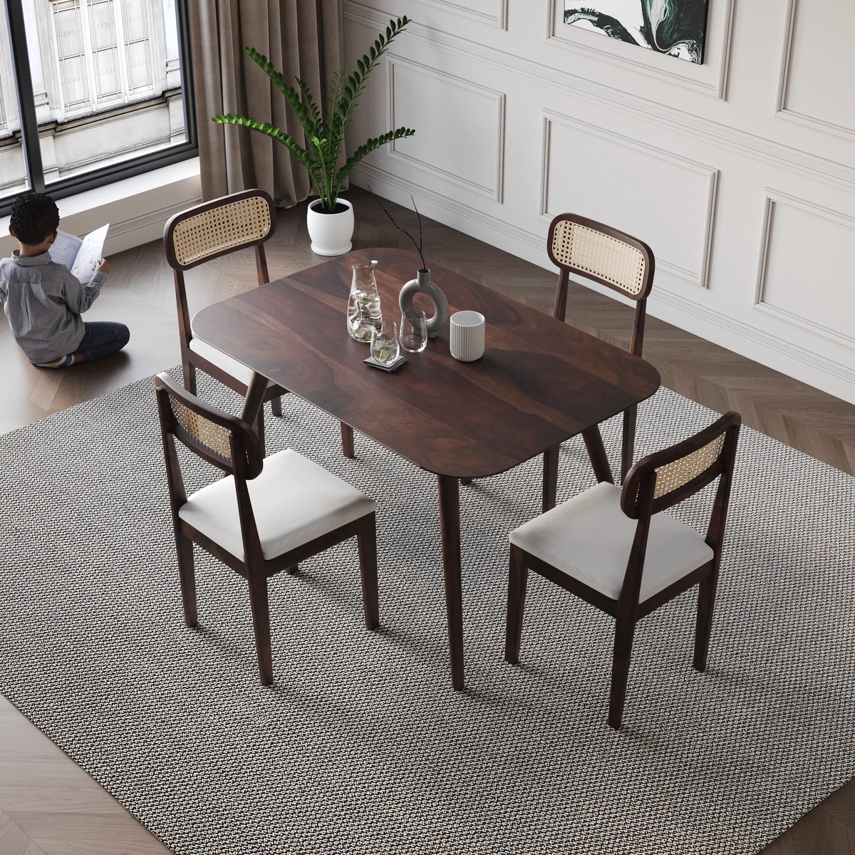 Dining table set with chairs in a room with a person reading by a window.