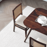 Wooden dining table with chairs on a white rug in a room with wooden flooring.