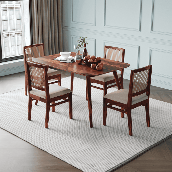 Wooden dining table with four chairs in a room with white walls and a window.