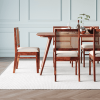 Dining table with wooden chairs featuring wicker backrests in a room with light blue paneled walls.