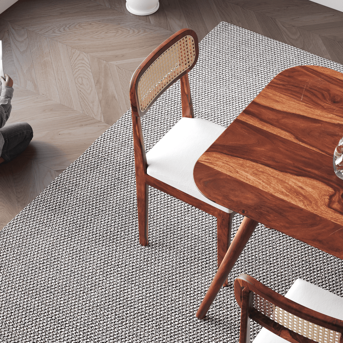 Wooden chair with woven backrest on a textured rug next to a wooden table.