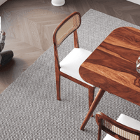 Wooden chair with woven backrest on a textured rug next to a wooden table.