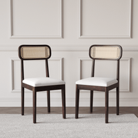 Two wooden chairs with wicker backrests and white cushions on a neutral background